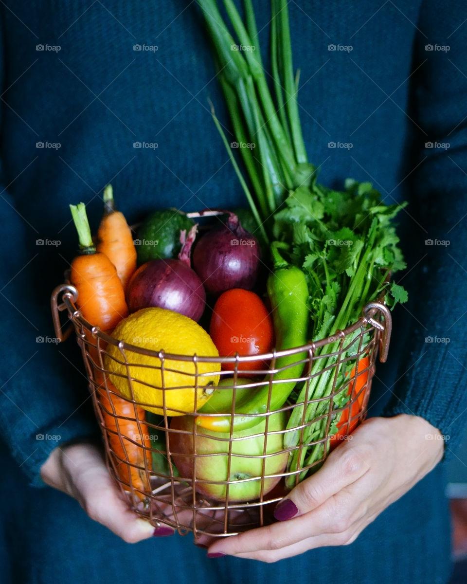 Mid section of woman holding basket with vegetables and fruits