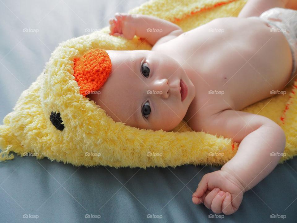 Baby laying in duck towel on bed