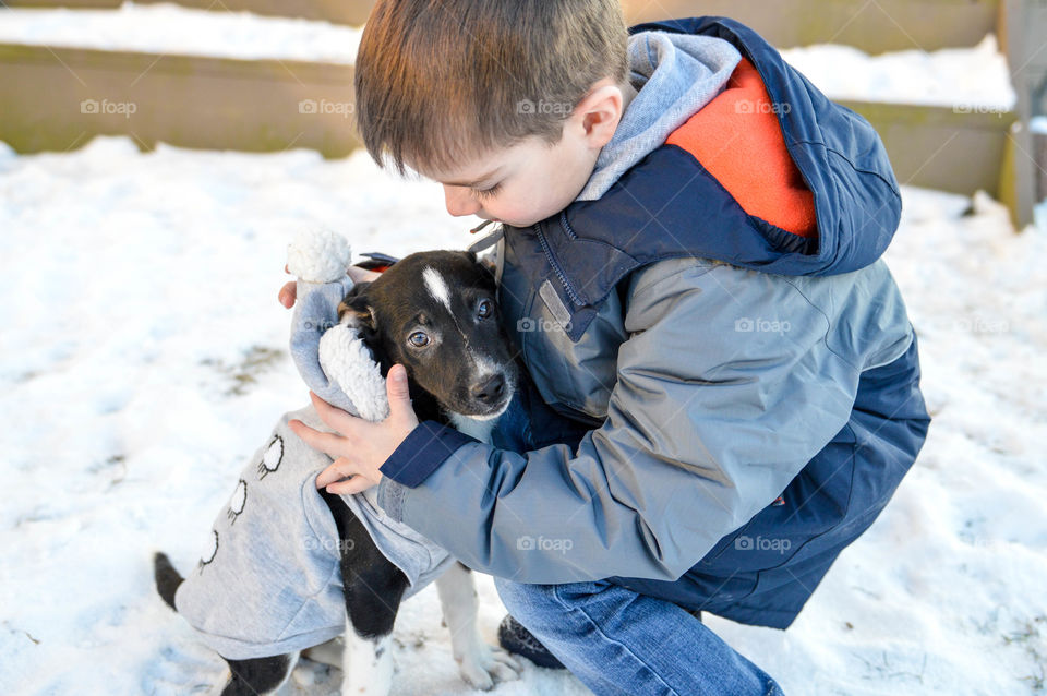 Young boy hugging his new puppy in the snow during winter