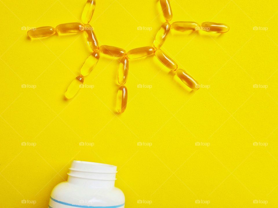 Omega3 and vitamin D capsules draw a sun on a yellow background