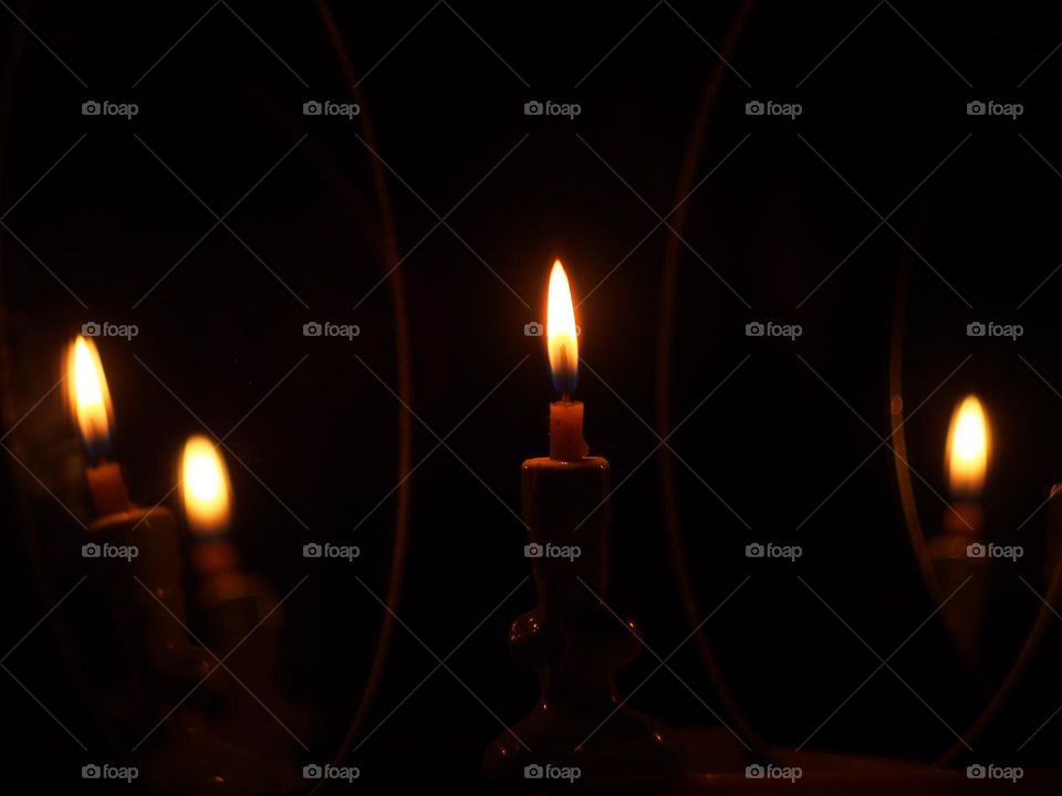 A candle burning in the dark is reflected in the mirrors.
