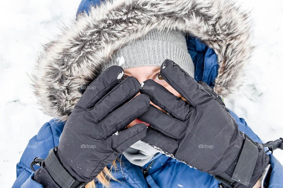 Woman in the snow outdoors and covering her face with gloved hands 