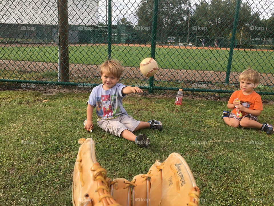 Brother sitting and playing at park against fence