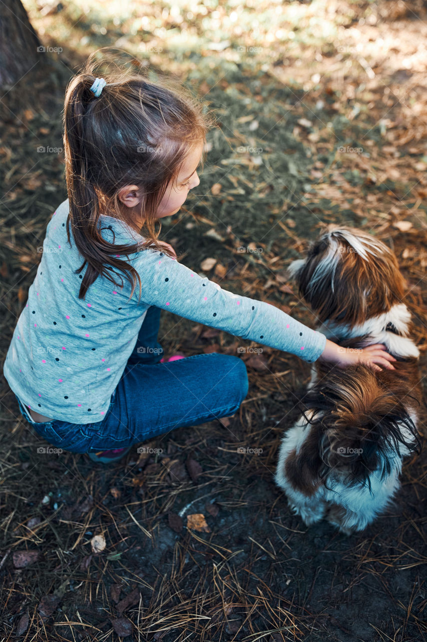 Little girl playing with her dog outdoors on summer sunny day