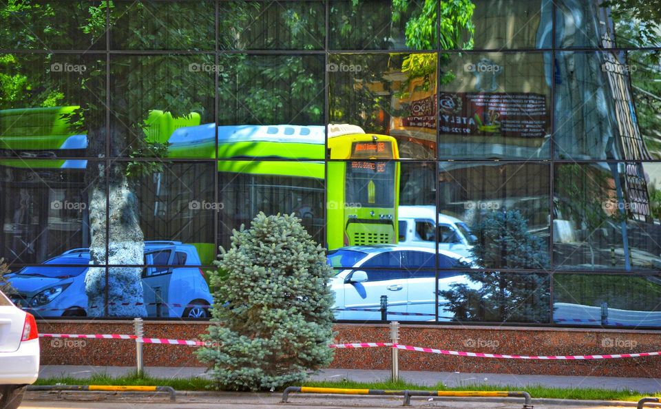 green city bus in the reflection of the glass of the building