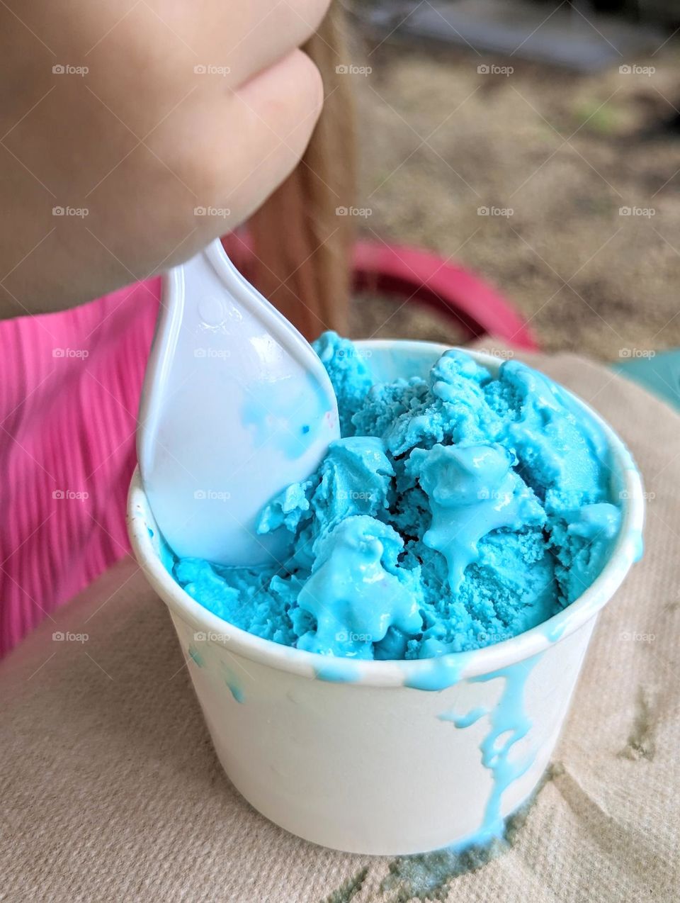 eating bright blue ice cream with bright pop of barbie pink clothes and chair in the background