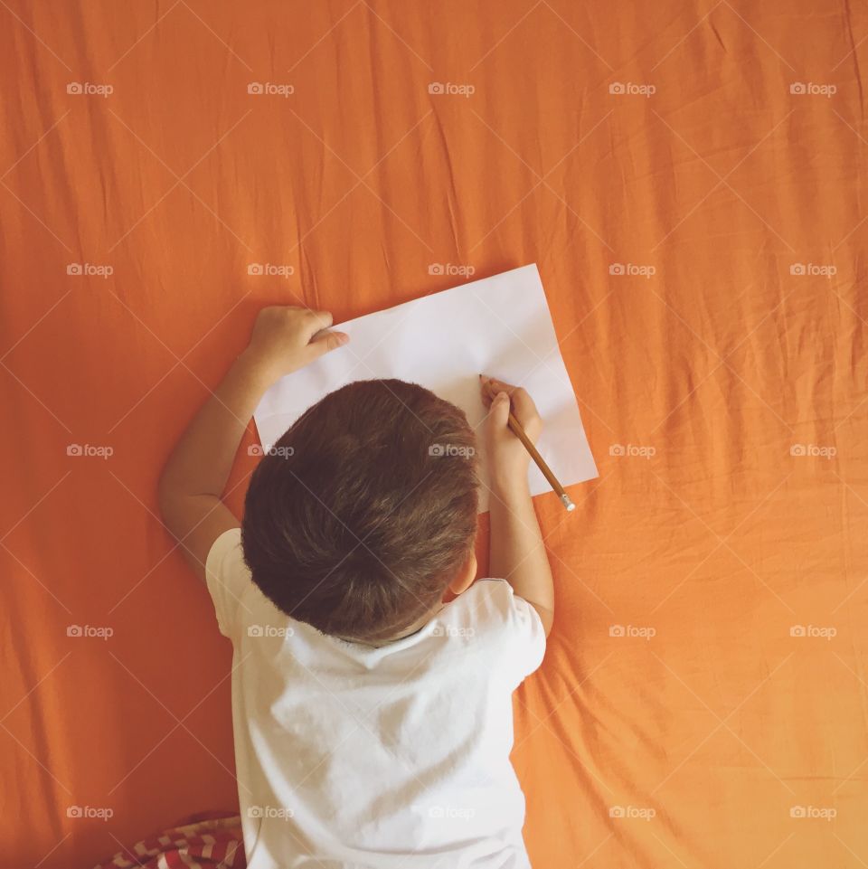 Boy lying on bed with paper and pencil