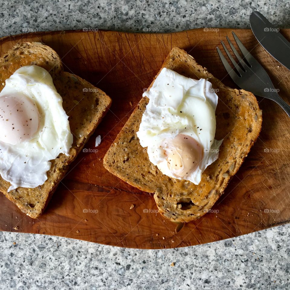 Poached eggs on toast on olive wood with cutlery 