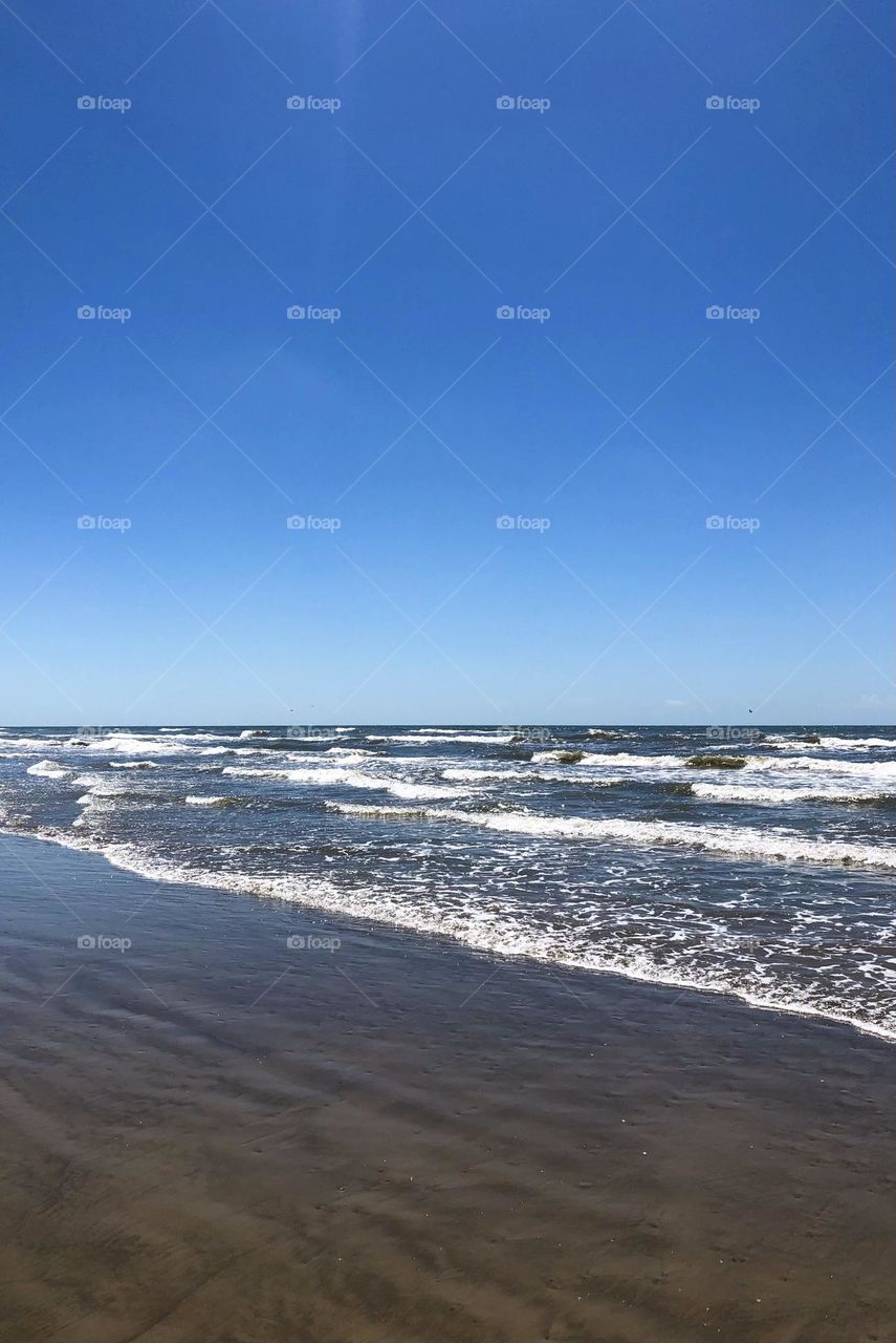 Best shot I can get in Galveston Texas. Small waves coming ashore against the bright blue sky. 