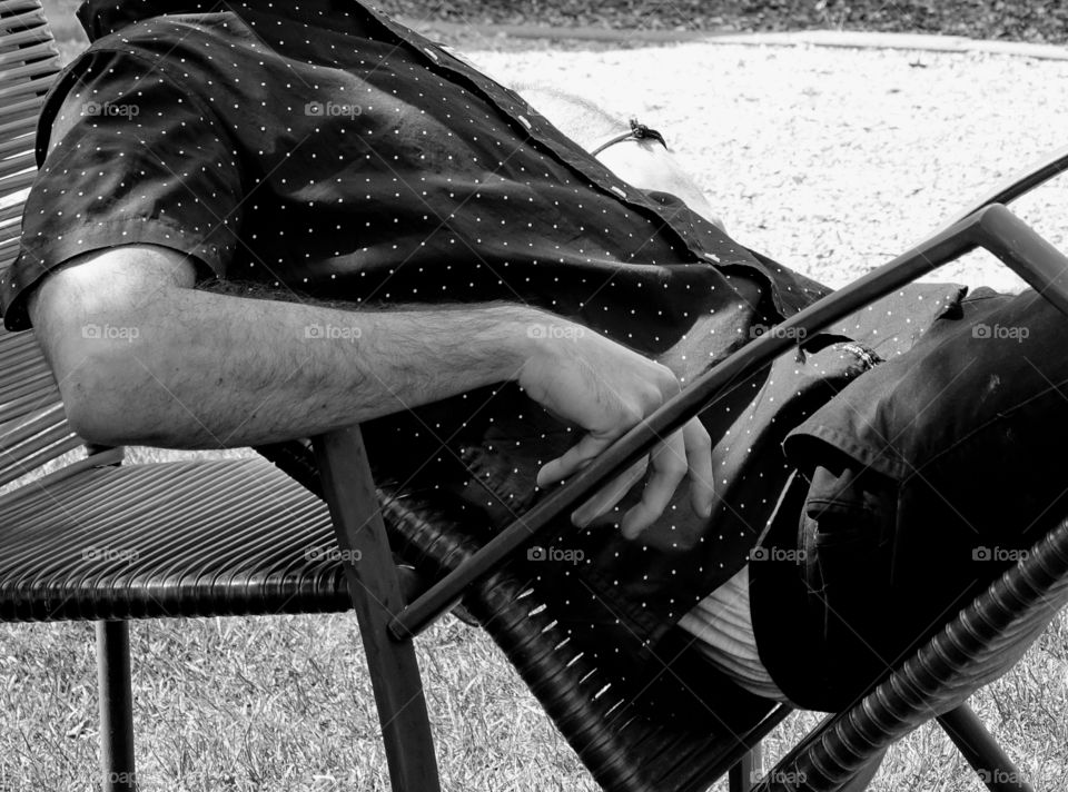 A young man leans back in a chair to relax outside. 