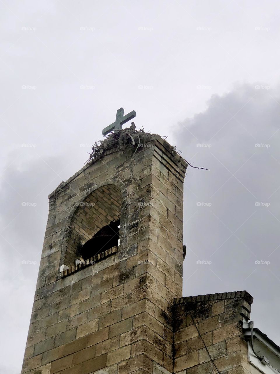 Looking up at church steeple and bell tower against an overcast sky. An osprey nest is visible against the cross on top.