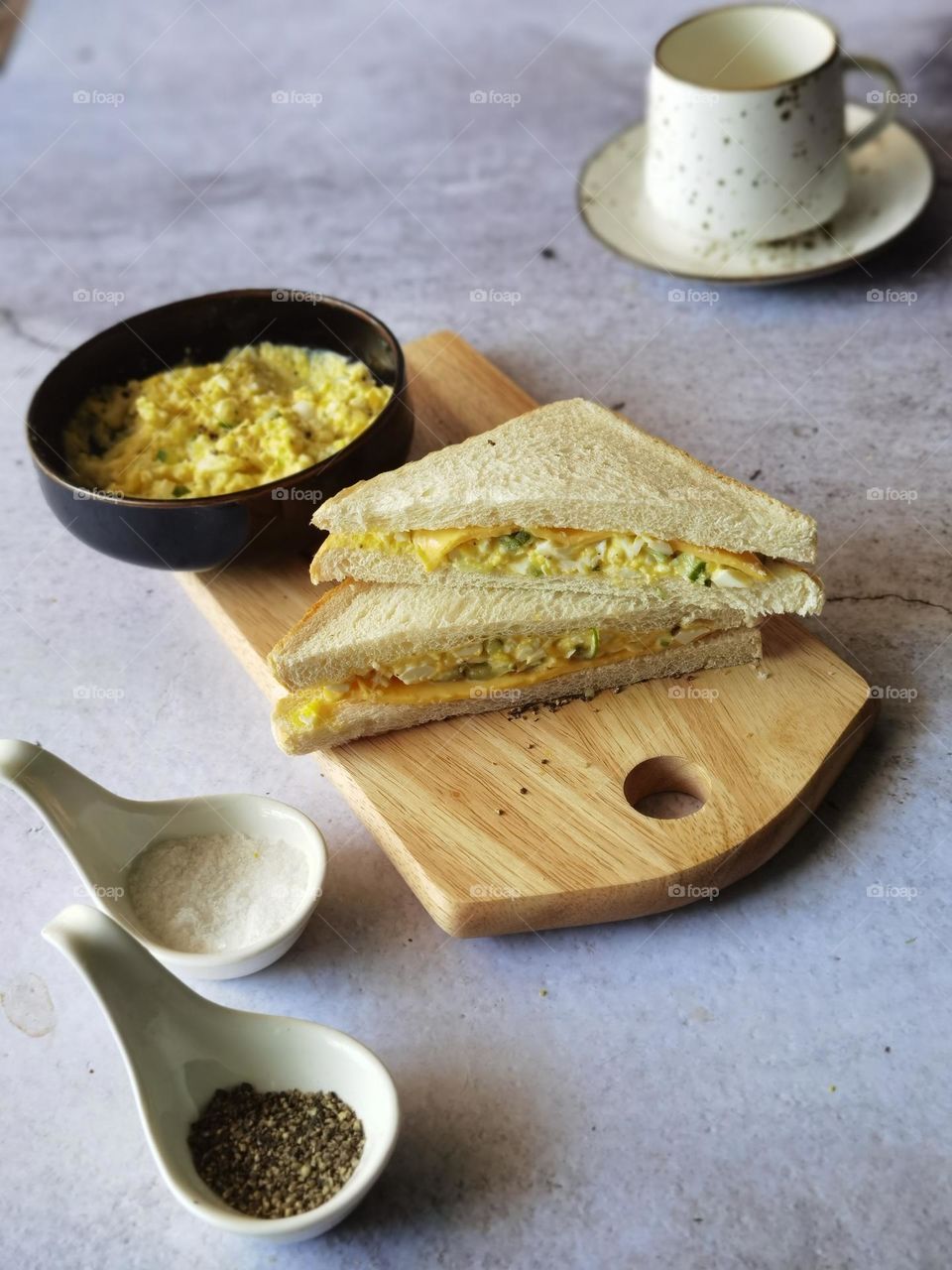Egg sandwich ready on a wooden board and some scrambled egg in a bowl