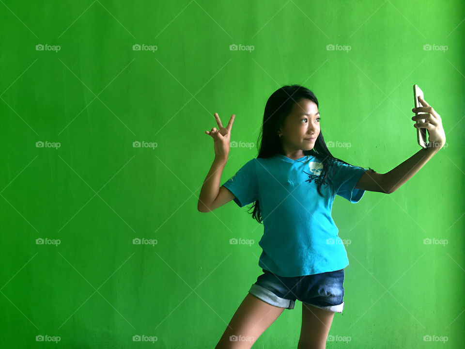 A girl snapping selfy at the green background