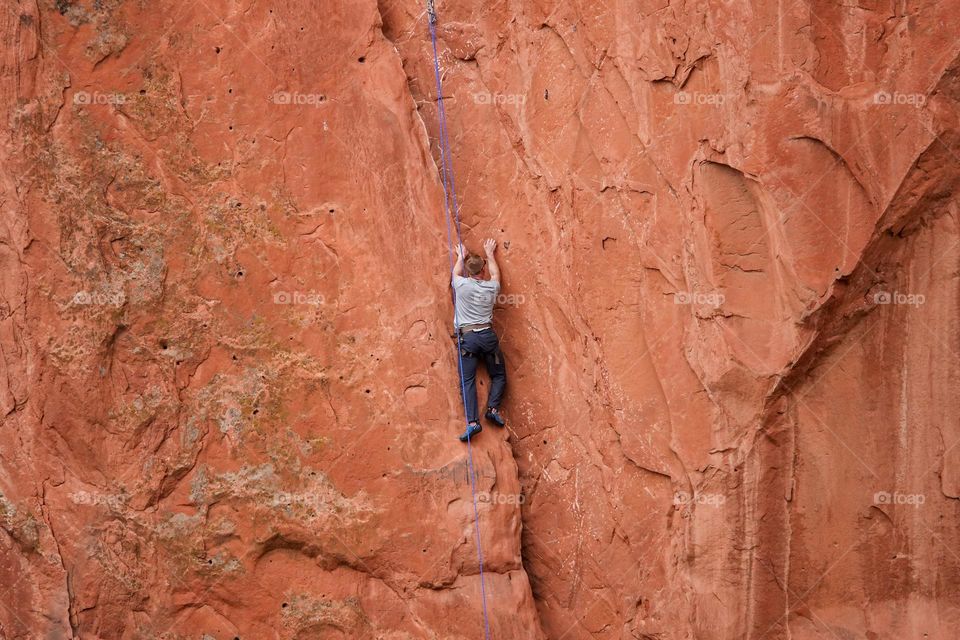A rock climber makes a difficult ascent on a red rock face