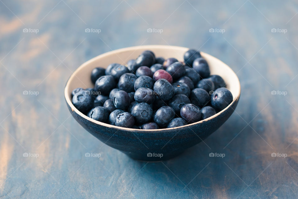 Small bowl full of fresh blueberries put on table painted in blue