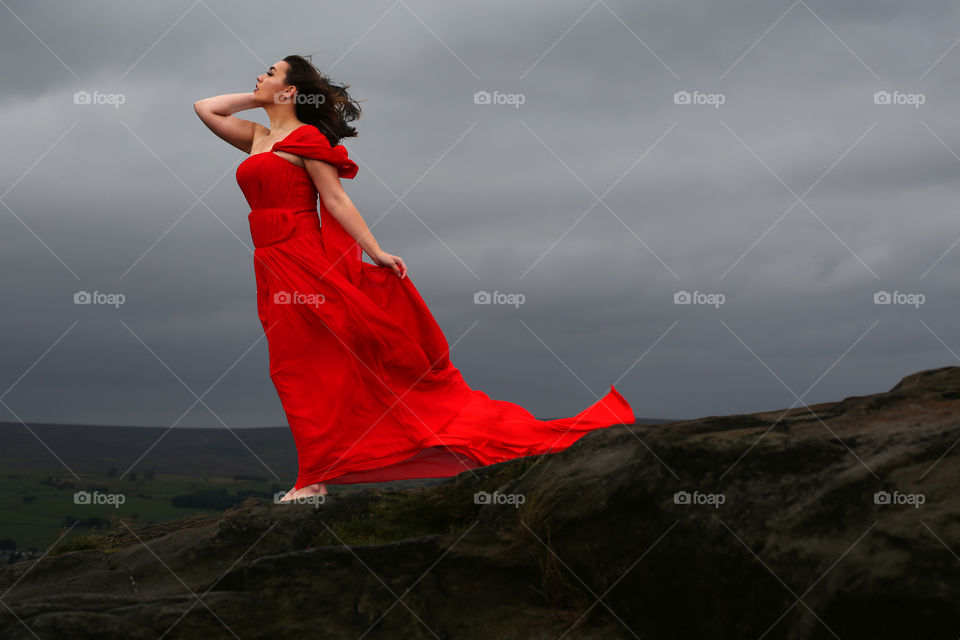Young woman posing on rocky mountain in red dress