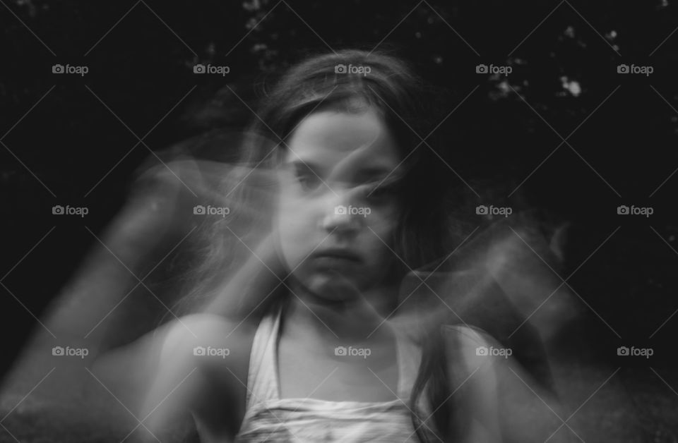 Black and white double exposure photo of a little girl moving her hands in a dark and somewhat creepy fashion. 
