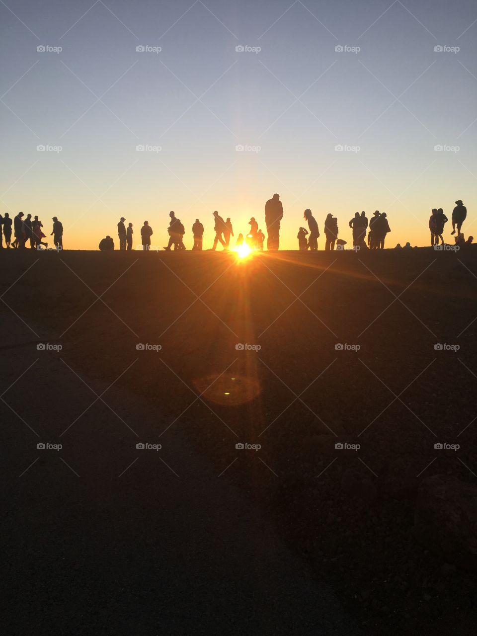 A group of people stand along a mountain ledge, silhouetted by the sunset.