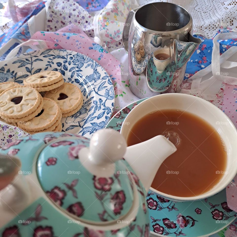 pretty teapot pouring english tea into a cup. biscuits, jug, bunting. hot drink