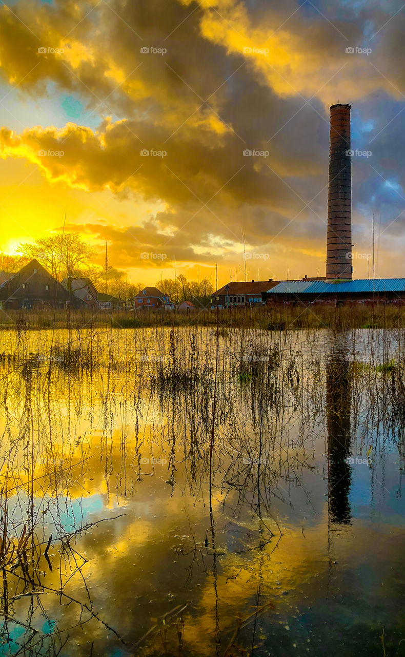 Dramatic and colorful sunset and ruins of an old stone factory reflected in the water of a puddle in the grass