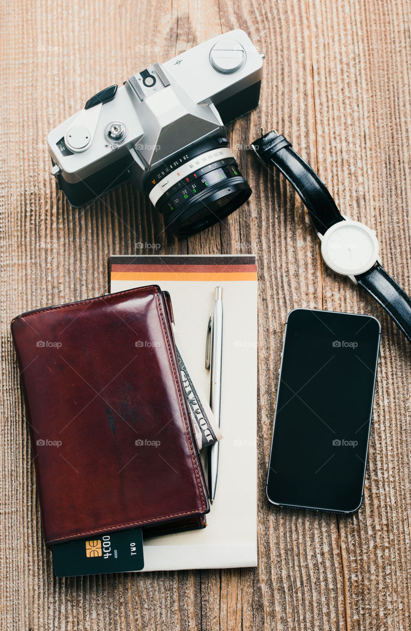 Smartphone with blank screen, camera, wallet, dollar banknotes, debit credit cards and notebook on wooden table. View from above. Portrait orientation