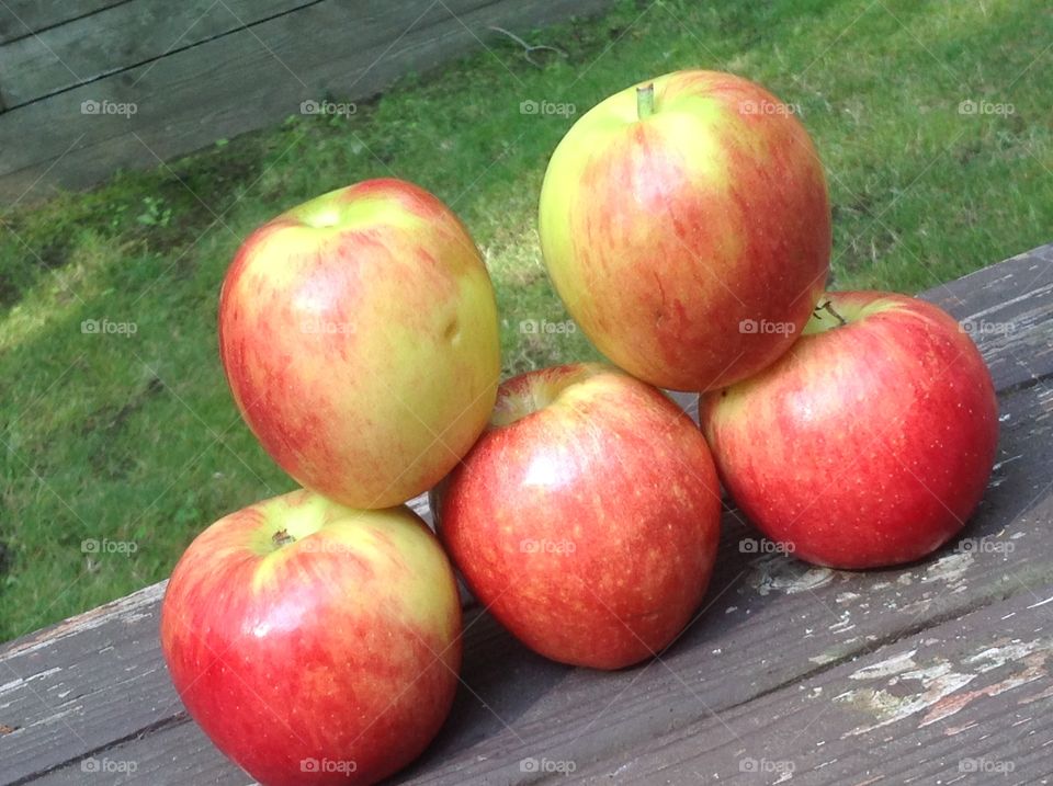 Apples stacked outdoors on wooden bench.