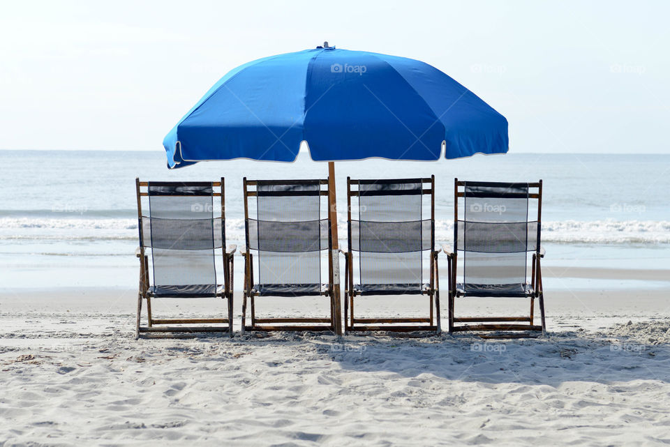 Lounge chairs lined up with an umbrella on the beach overlooking the ocean