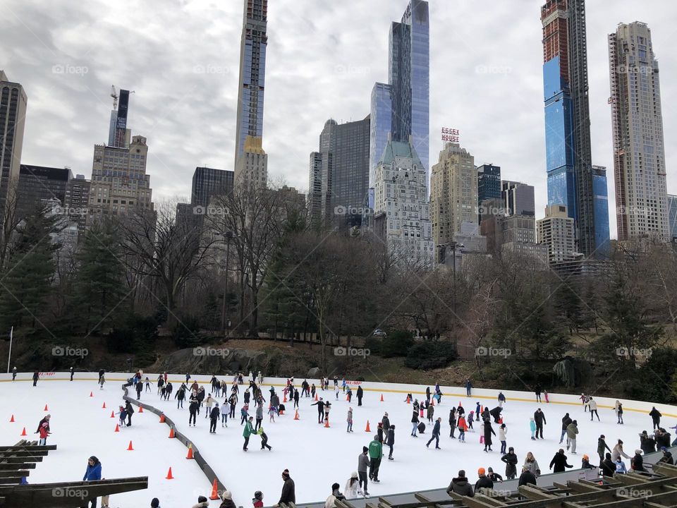 crowd of people ice skating in New York's Central Park surrounded by skyscrapers