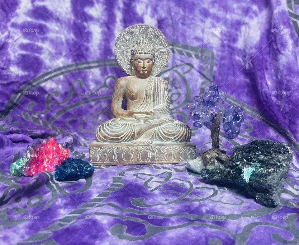 A Buddha meditating with crystals, and a calming purple background.
