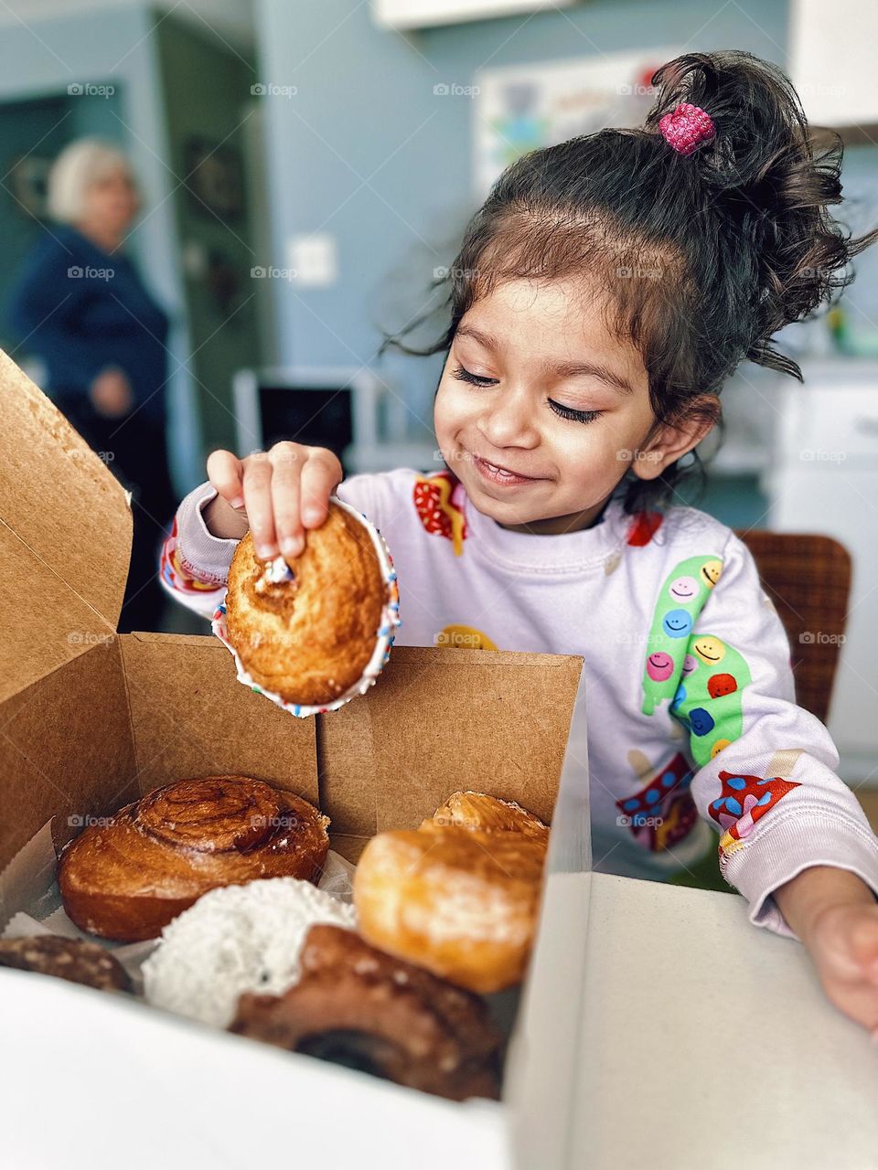 Toddler selects a donut from large box of donuts, cute toddler is happy about eating donuts, toddler grabs donut, eating donuts for breakfast, portrait of a toddler, happy toddler eating sugar, mobile photography, portraits with a smartphone 