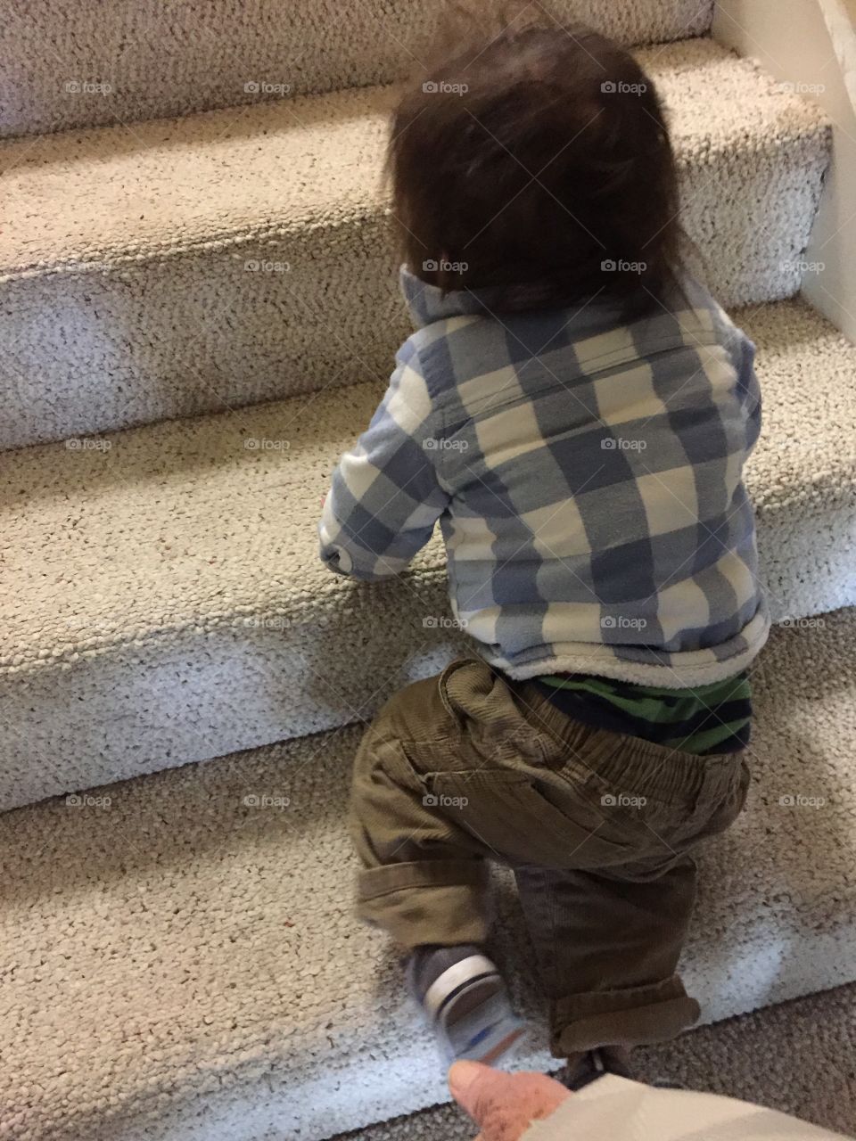 Baby boy climbing the stairs with his blue and white plaid jacket and tan corduroy pants. 