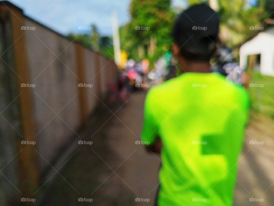 The image shows a farther wearing a green shirt outdoors, possibly on a street with trees in the background and the sky above and  waiting for his son's arrival