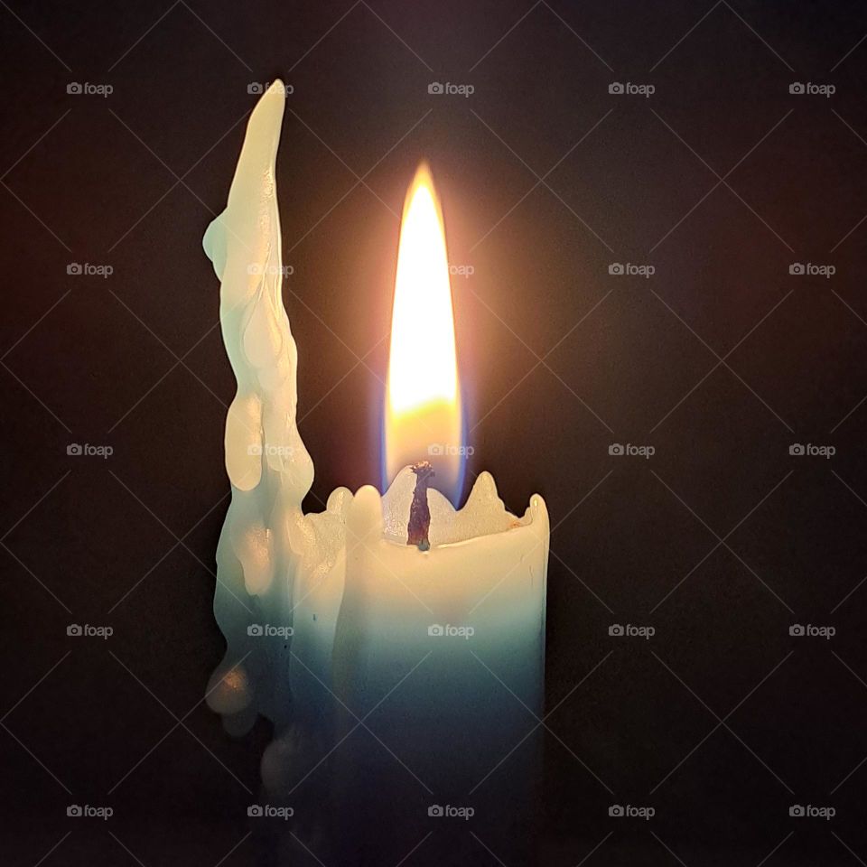 Blue birning candle in the darkness. melting wax, flame alight.