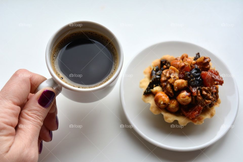 cup of coffee in the hand and cupcake on a plate on a white background, morning routine