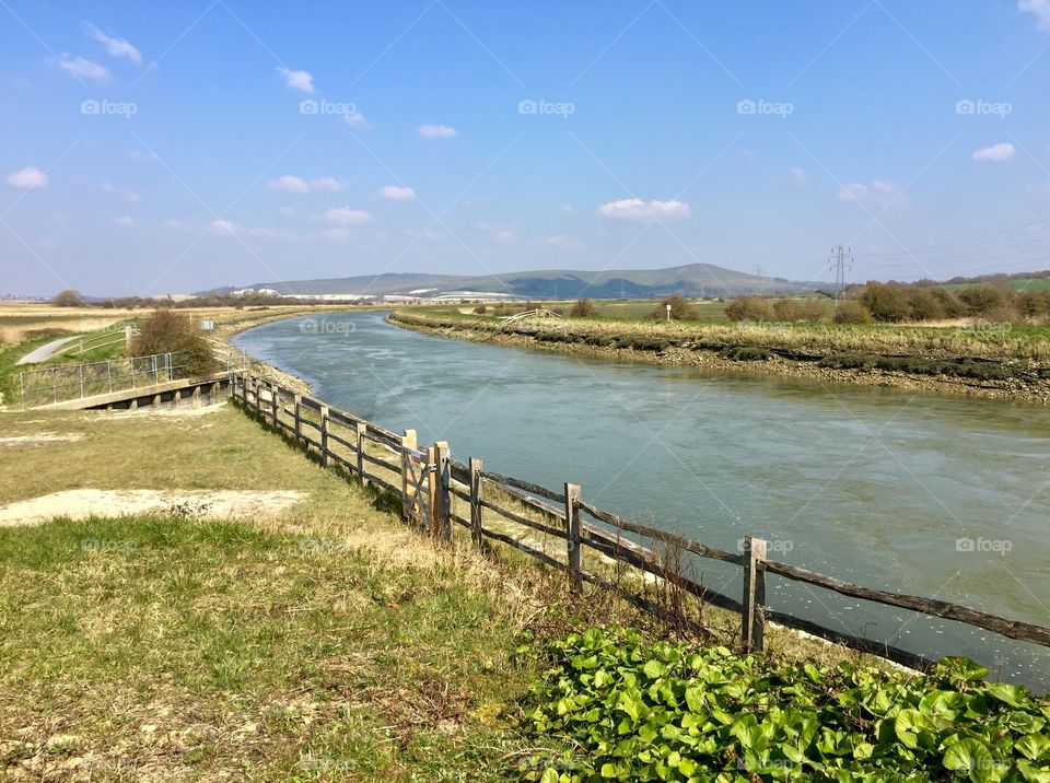 Flowing river within farmlands and blue sky with dotting clouds