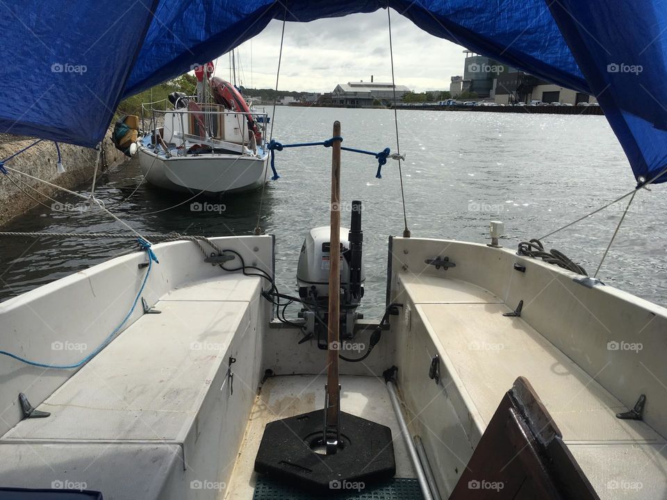 A view onto the East River at Newtown Creek in LIC, Queens, New York from aboard our sailboat, the „Salvation“ looking out from the cabin with a lounging area onto the front deck. A blue tarp covers the outside deck area. 2018. Hypnotic Productions