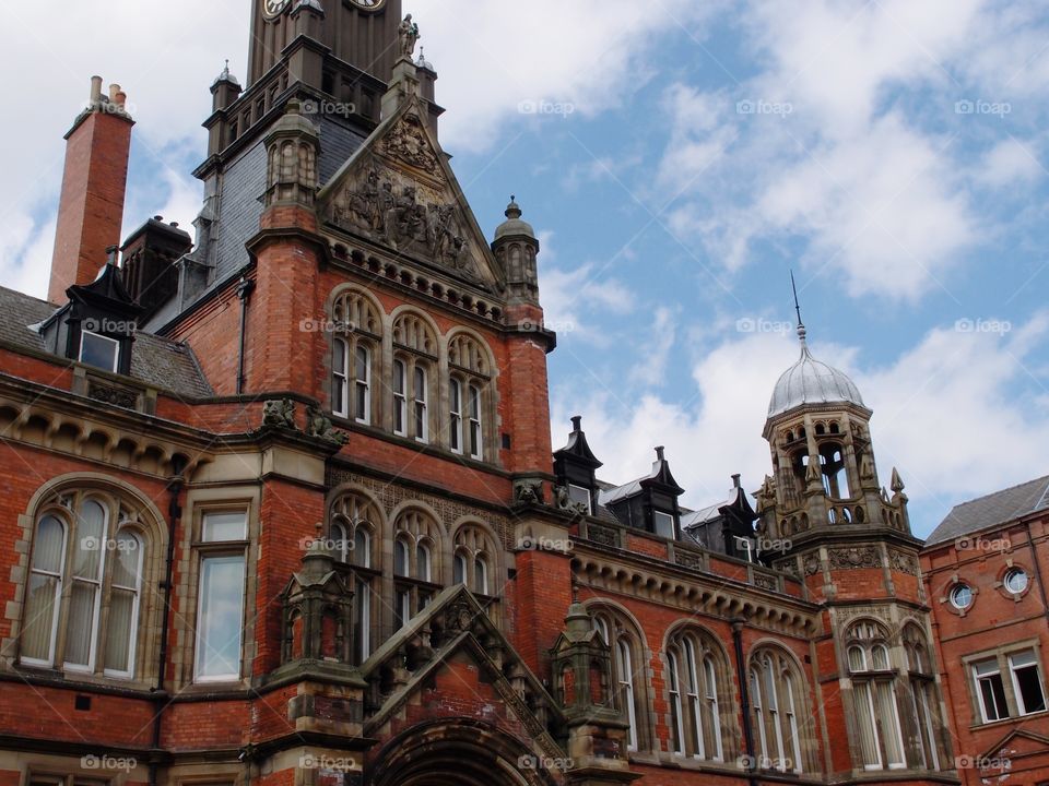 A beautiful intricately designed old brick building with lots of windows and a clock tower on a nice summer day in England. 