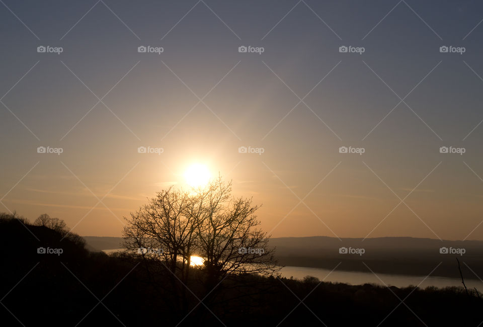 Beautiful sunset on Danube River. Orange color of the sky. Reflection on the river. Sun and tree.