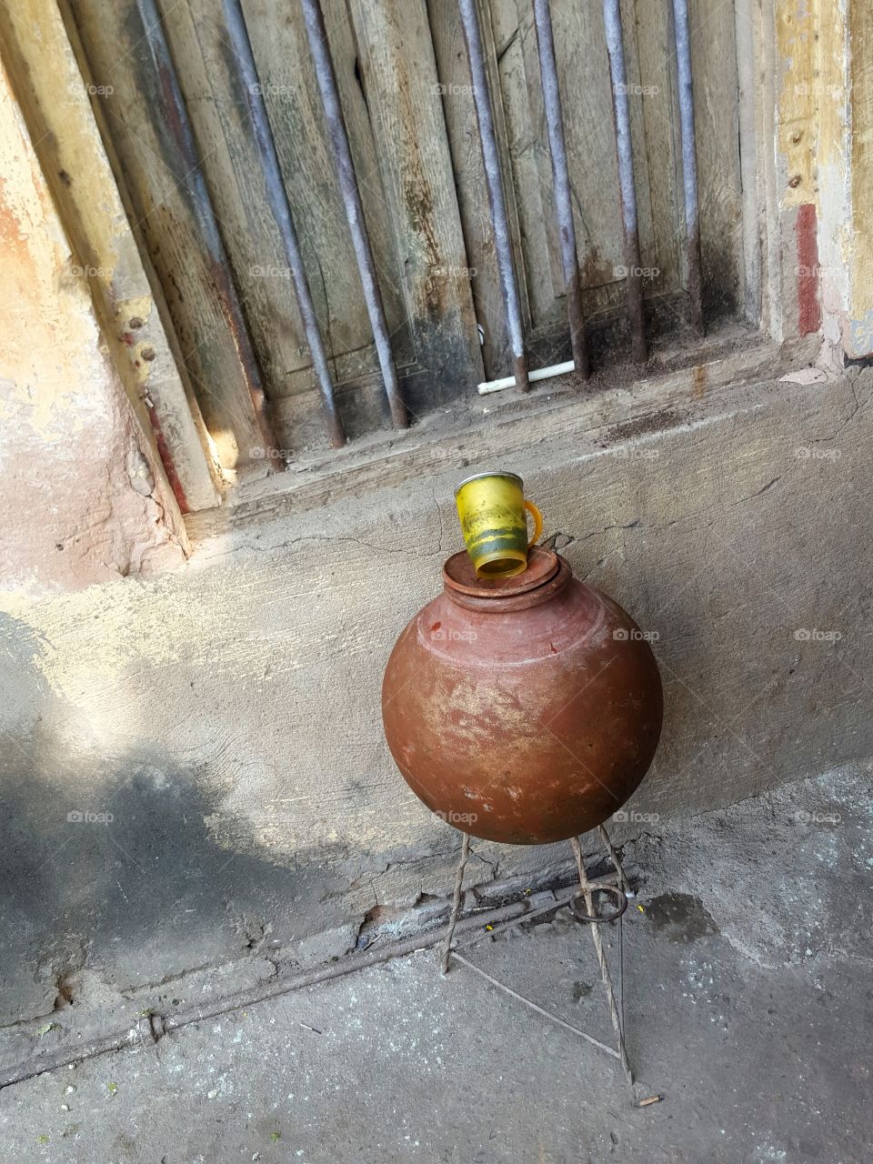 Earthen Indian Clay pot for water with yellow mug and window in the background