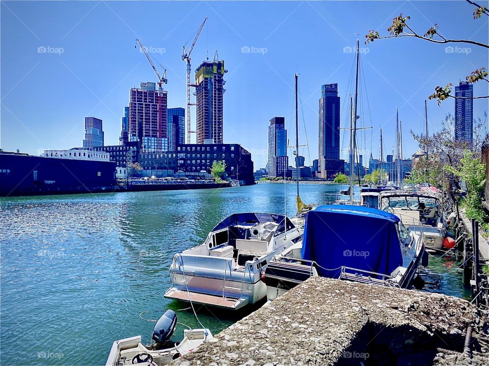 A panoramic view of „Newtown Creek“ with its picturesque beautiful boats, sailboats, masts and the shimmering bright blue waves of the East River on a sunny afternoon in May, 2022. Hypnotic Productions