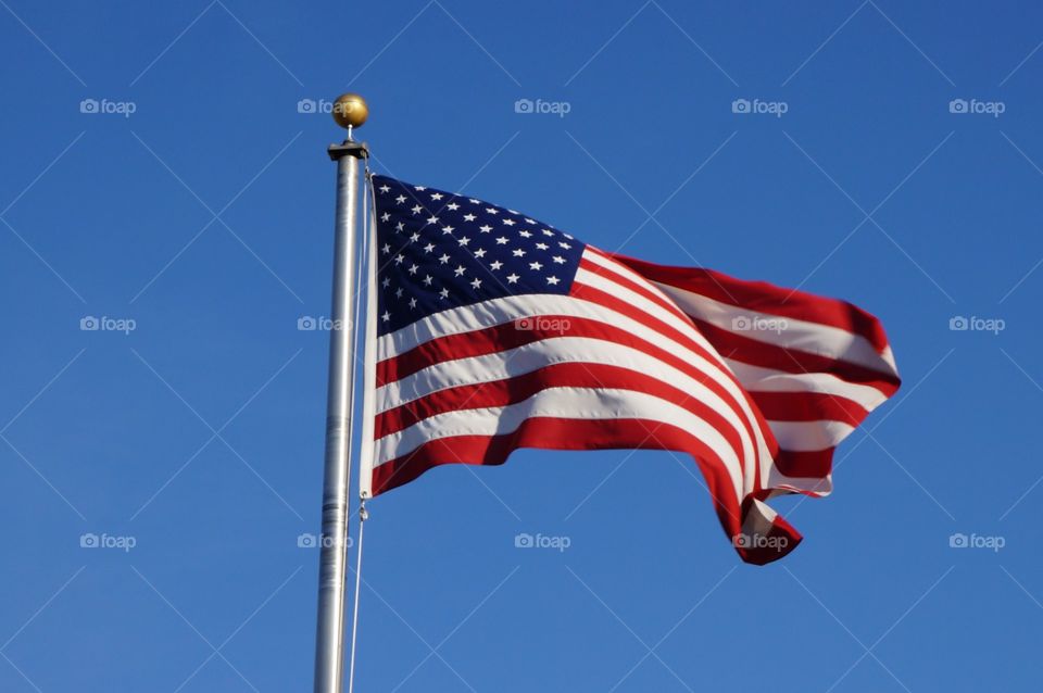 AMERICAN flag blowing in the wind with a blue sky.