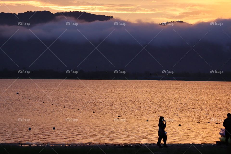 A person walking by the shoreline with beautiful scenery of sunset