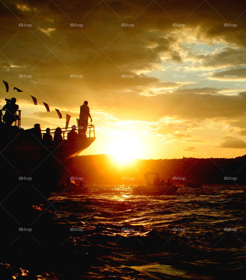 Closing of sea procession in my town at sunset, for a traditional summer festival in my town. A man observes horizon while tourists admire sunset. Picture taken from a little boat.