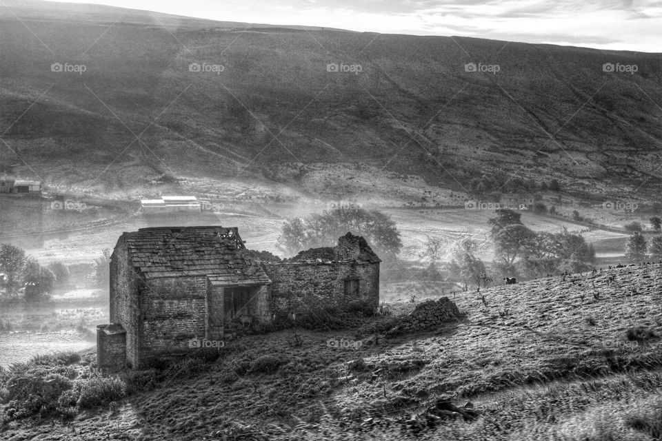 Deserted Far Barn. A black and white image of a deserted and derelict barn in a farmer's field with a deep valley behind.