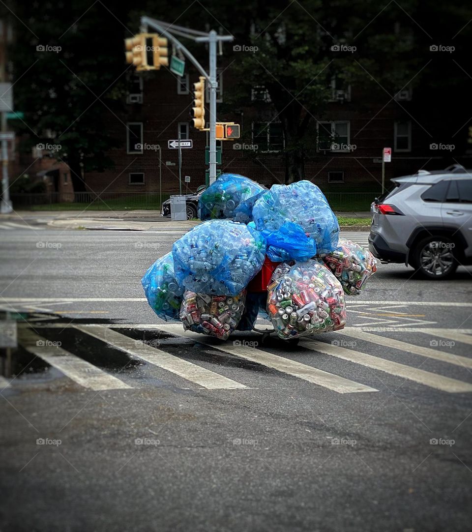 Cart with bags of recyclables being wheeled across a city street intersection 