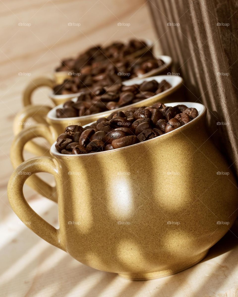 A row of 4 coffee cups, filled with coffee beans against a wood background with shadow lines across them 