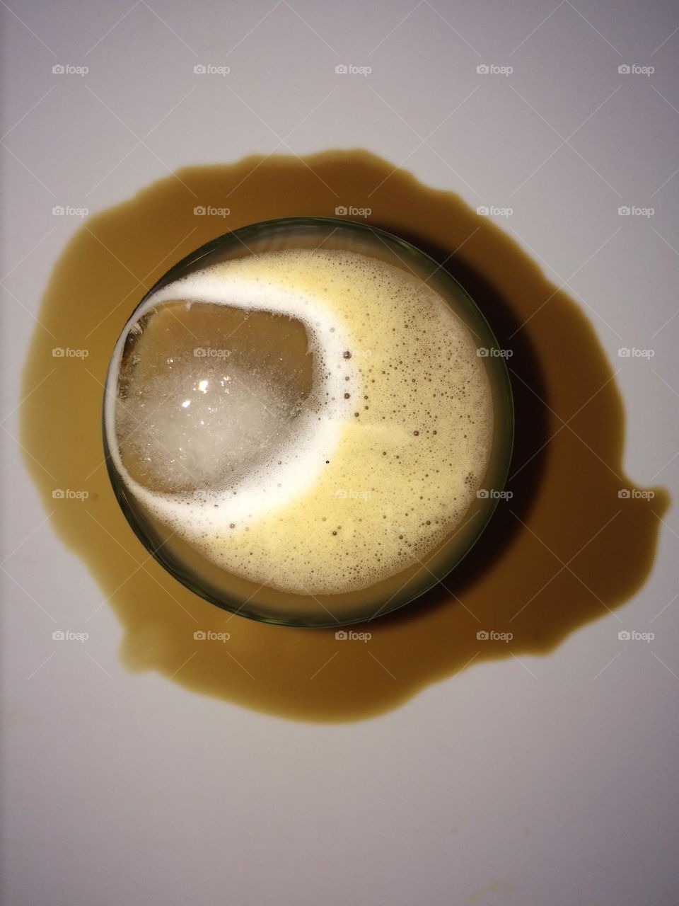 Glass of iced coffee sitting in spilt coffee puddle