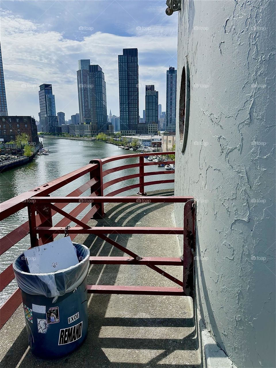 The orange red of the “Bauhaus” inspired metal railing of the “Pulaski Bridge” that connects LIC to “Greenpoint”, Bklyn meets its complementary color blue in the “E River”, the LIC and “Manhattan” skyline and the sky above. 2025. Hypnotic Productions