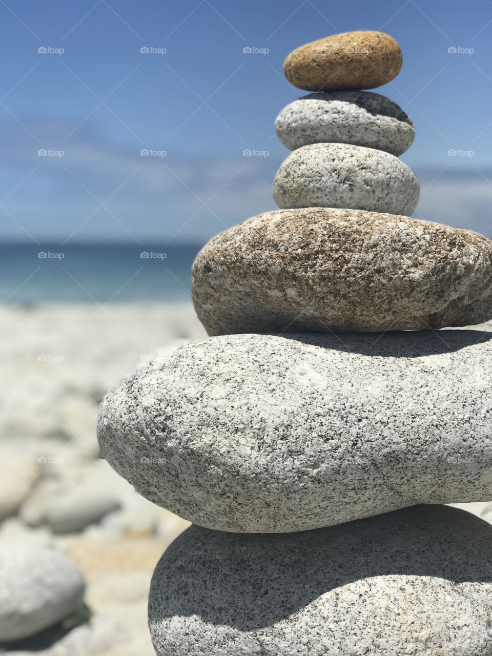 Zen. A closeup of stones delicately balanced, framed by calm ocean waves brushing the shoreline. 