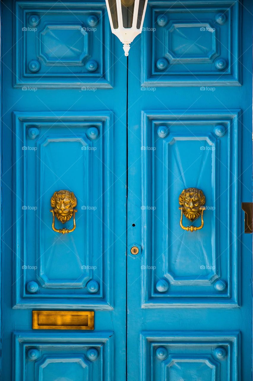 A beautiful turquoise doorway with golden lion head knobs, in the village of Rabat, in Malta.